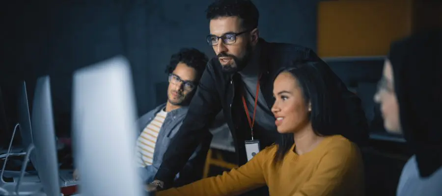 Group discussion with diverse colleagues in a dark office setting.